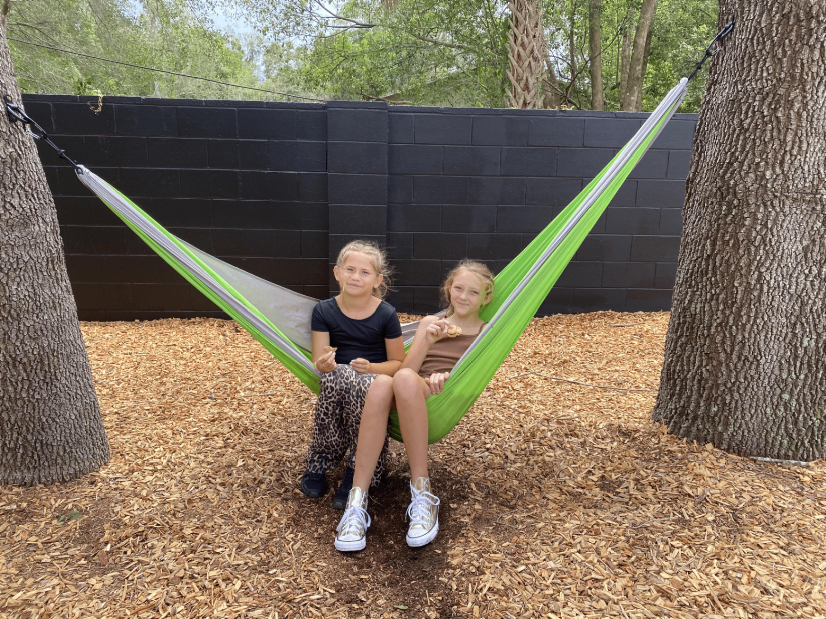 Two smiling school age children relaxing together in a bright green hammock outdoors